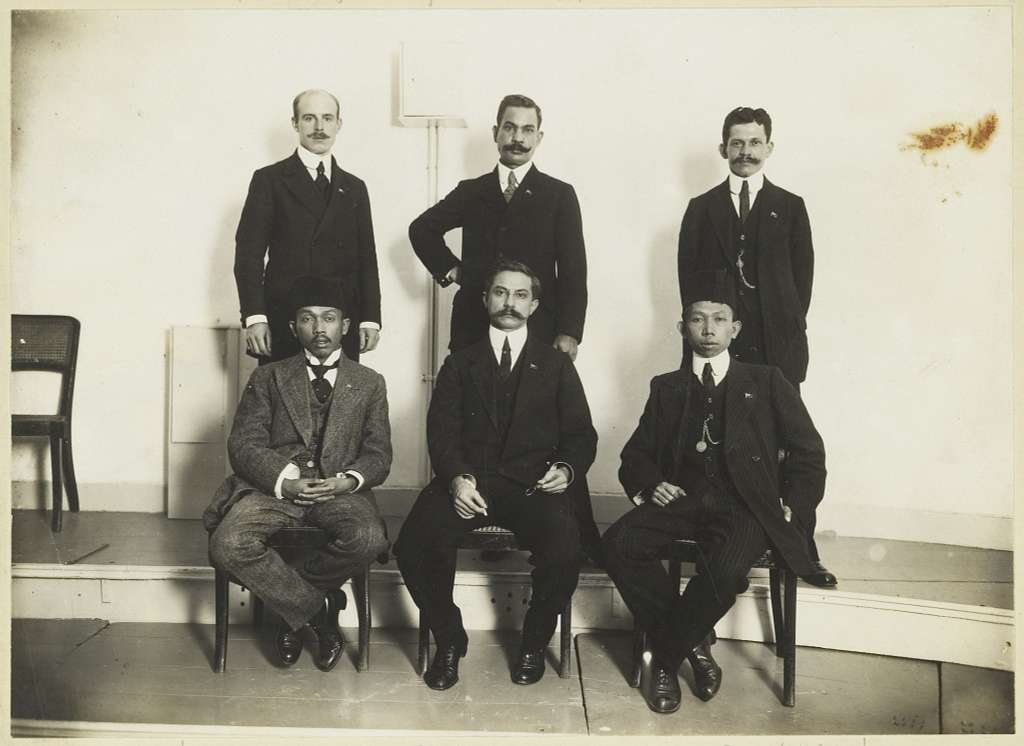 Pada tahun 1913 di Den Haag, Belanda, anggota Indische Partij berpose untuk foto. Di barisan depan, dari kiri ke kanan, terlihat Tjipto Mangoenkoesoemo, E.F.E. Douwes Dekker, dan R.M. Soewardi Soerjaningrat. Sementara itu, di barisan belakang, berdiri dari kiri ke kanan, adalah F. Berding, G.L. Topée, dan J. Vermaesen.