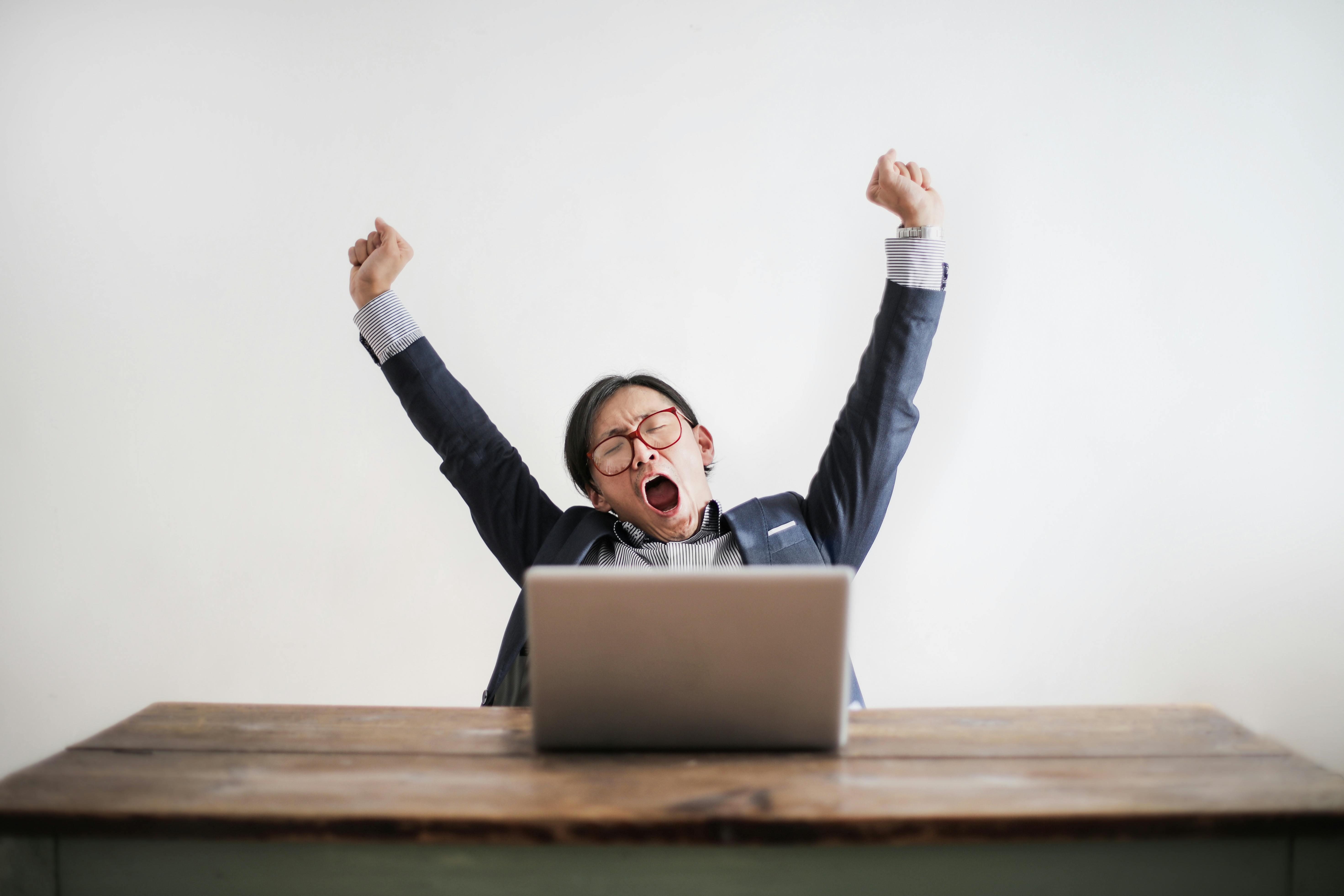 Photo of Yawning Man with His Hands Up and Eyes Closed Sitting at a Table with His Laptop | Photo by Andrea Piacquadio from Pexels