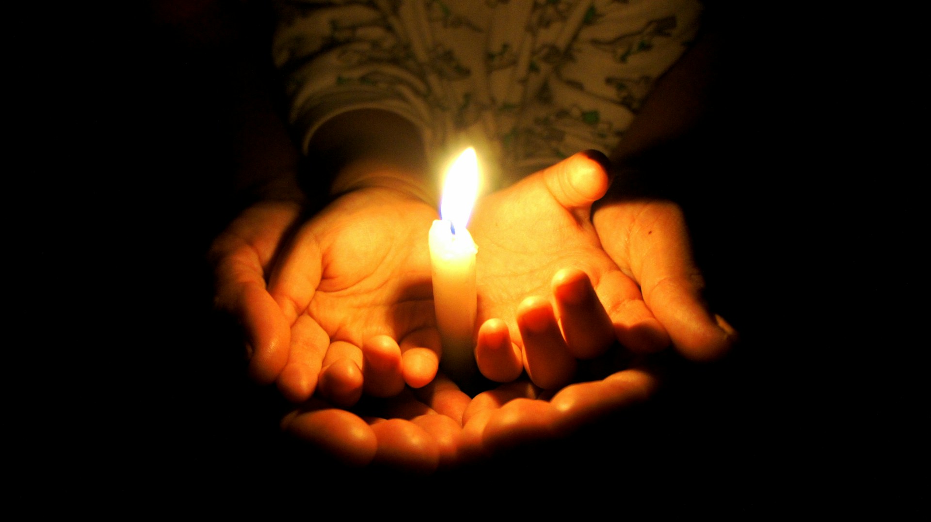 Lilin yang menyala dengan tangan di bawahnya | Candle in the dark (image: Diego Cespedes Cabrera, Unsplash)