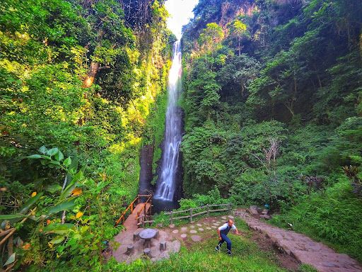 Gambar seseorang tampak berlari dengan background Air Terjun Putuk Truno