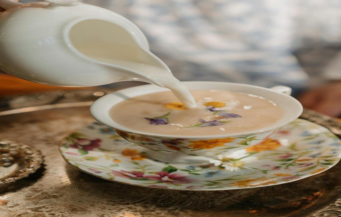 Teh susu di dalam gelas dan di atas piring putih dengan motif bunga.