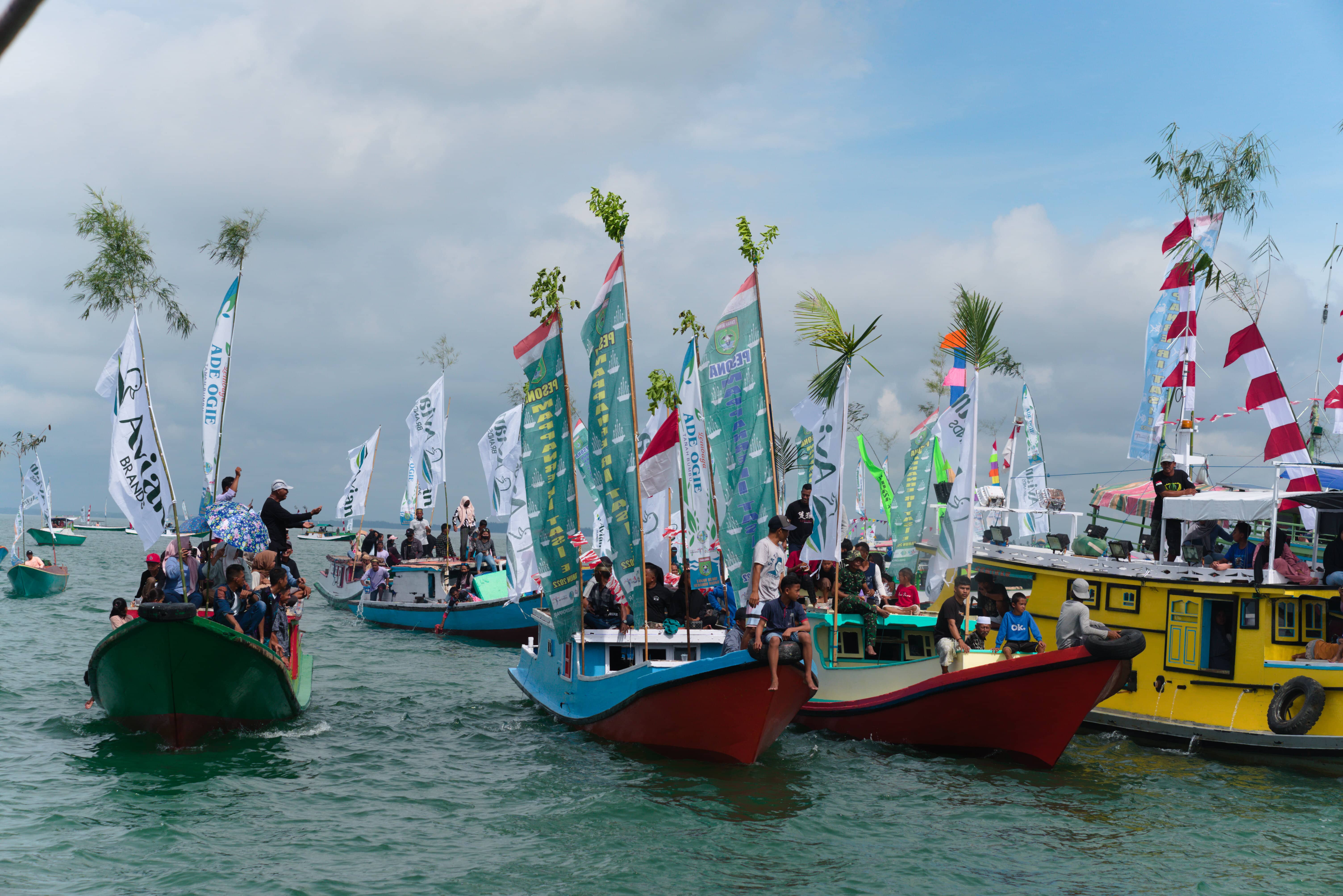 Foto beberapa kapal nelayan berhiaskan baliho untuk festival, siap berlabuh menuju lautan.