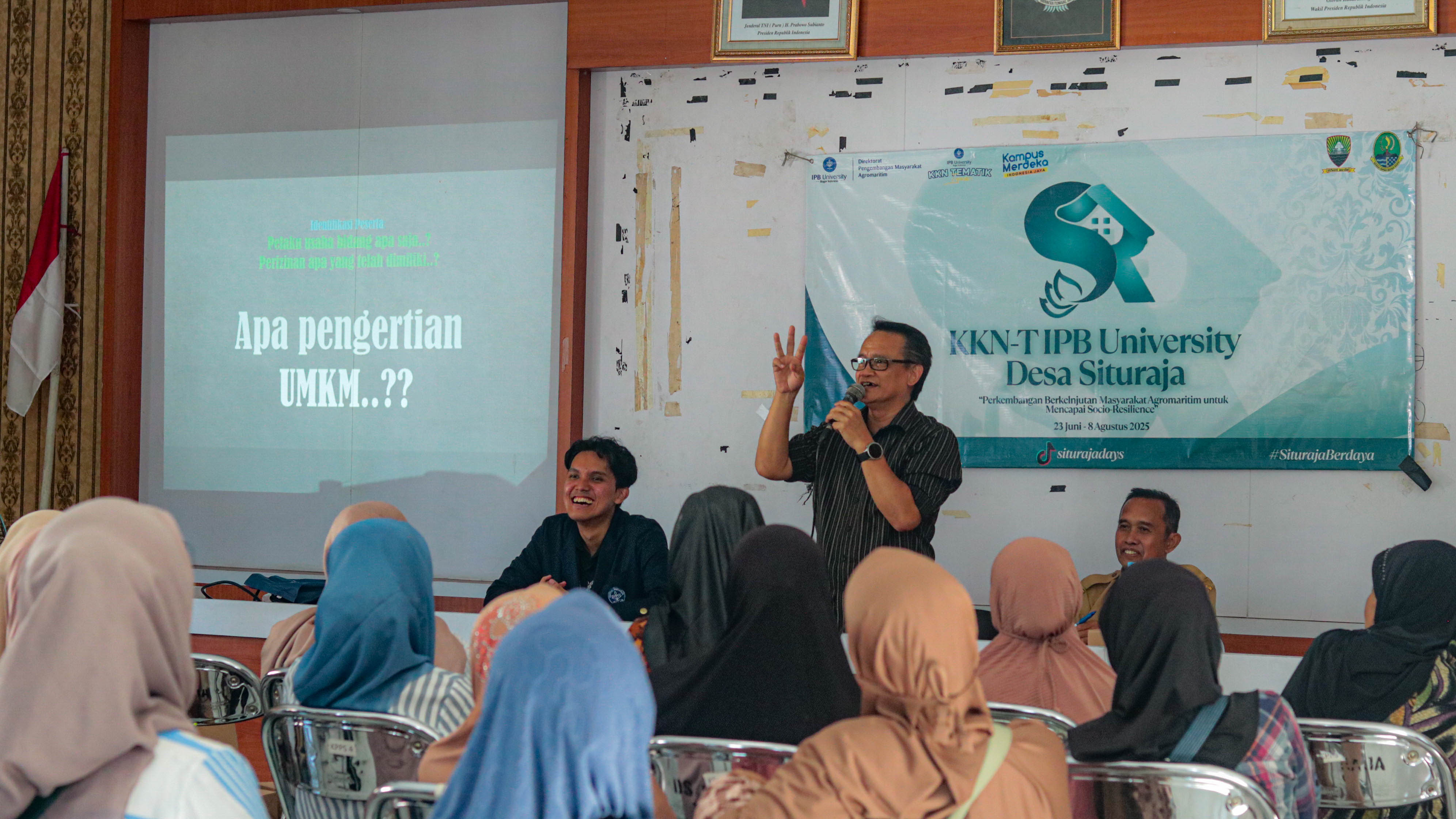 Seorang narasumber memberikan materi tentang pengertian UMKM dalam workshop bersama pelaku usaha lokal, didampingi mahasiswa KKN-T IPB University di Balai Desa Situraja, Sumedang.