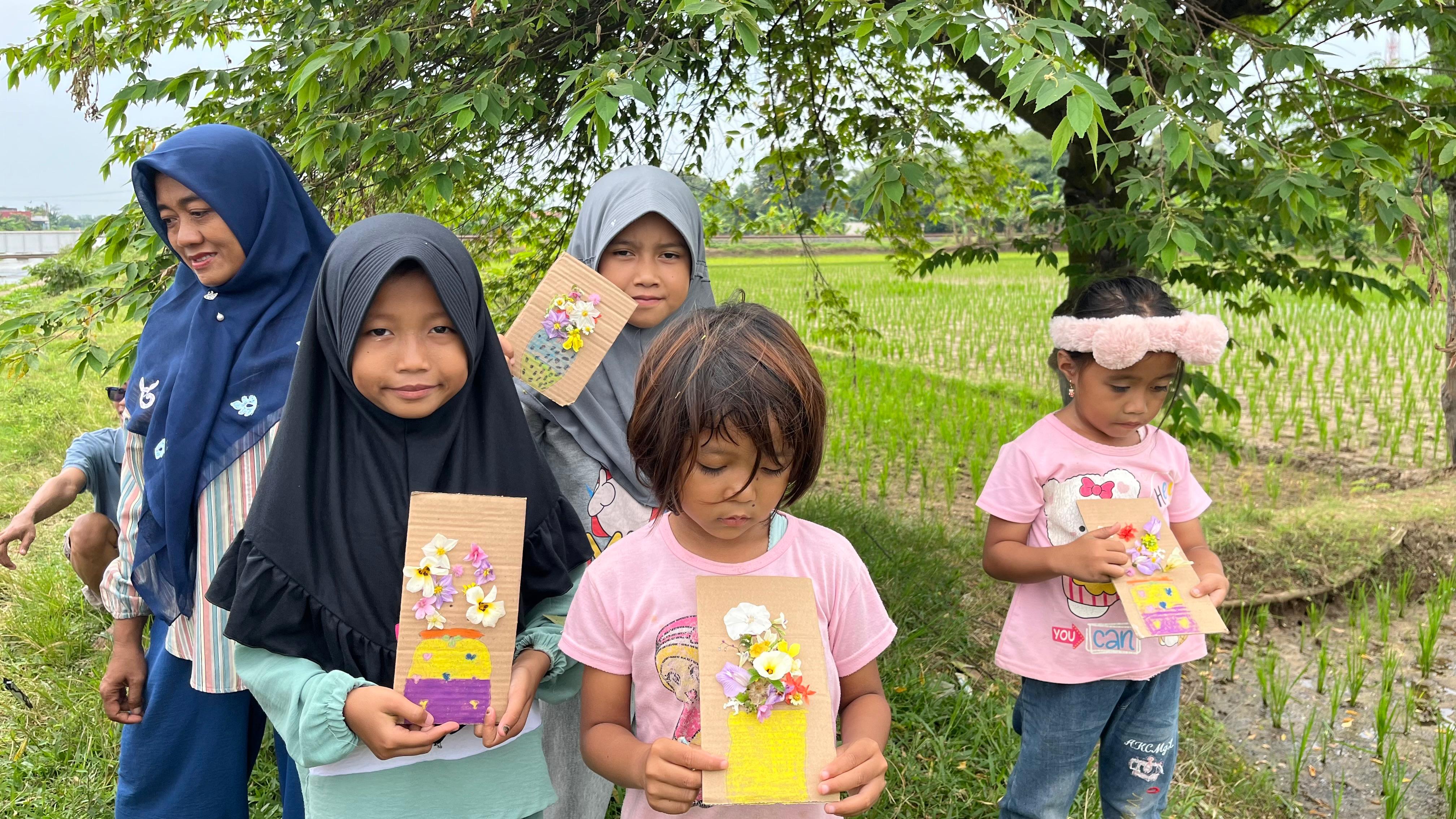 Anak-anak menunjukkan hasil karya vas bunga dari kardus bekas yang dihias dengan bunga segar.