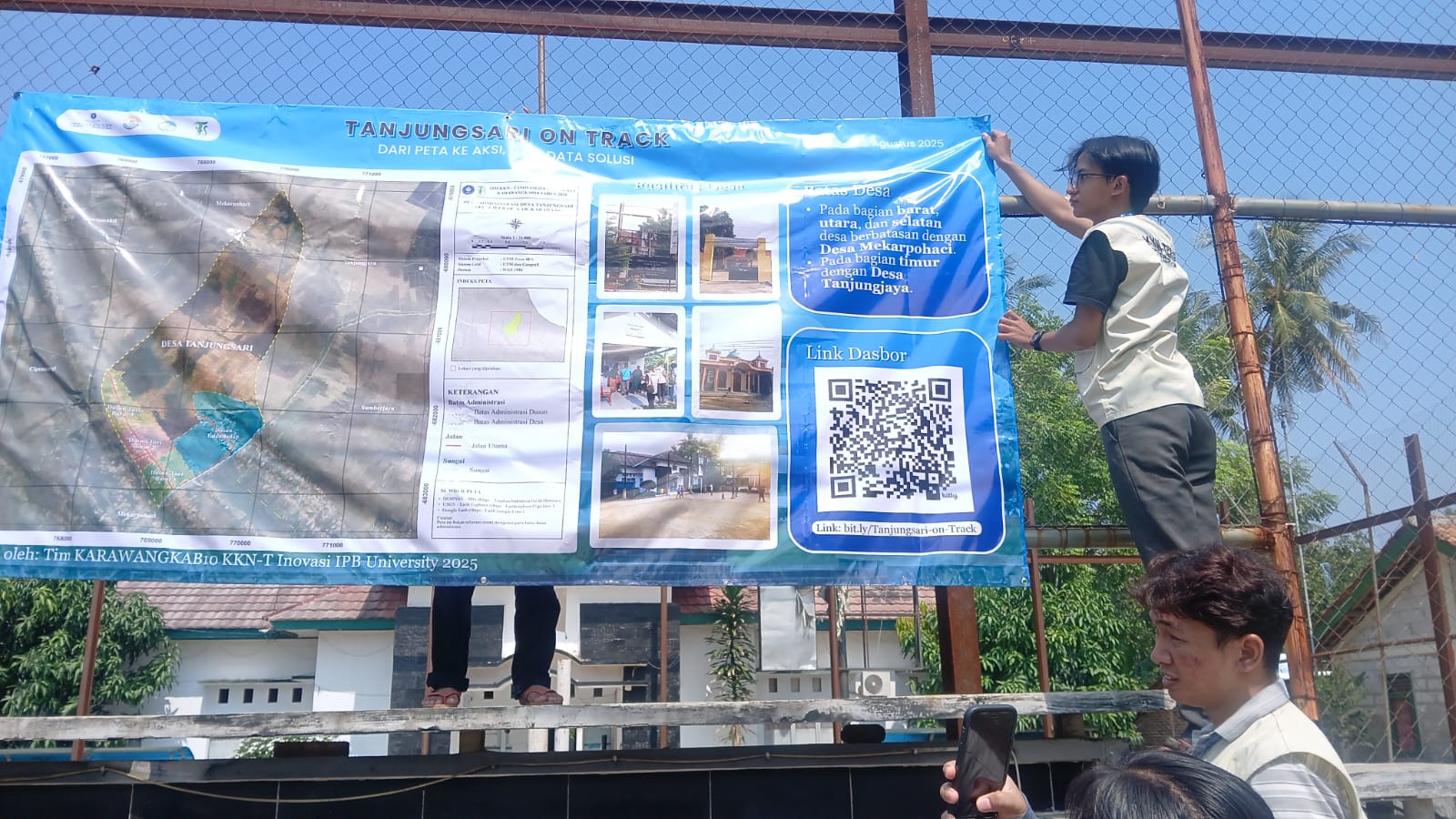 Foto anggota tim KKN-T Inovasi KARWANGKAB10 IPB University memasang banner di depan kantor desa
