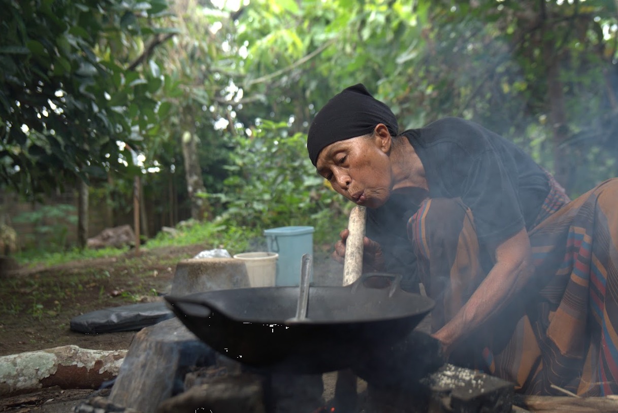 Seorang perempuan Minangkabau meniup bara tungku saat proses marandang, menjaga api tetap kecil agar Bareh Randang matang perlahan dan sempurna. Foto oleh Rekam Indonesia/GNFI
