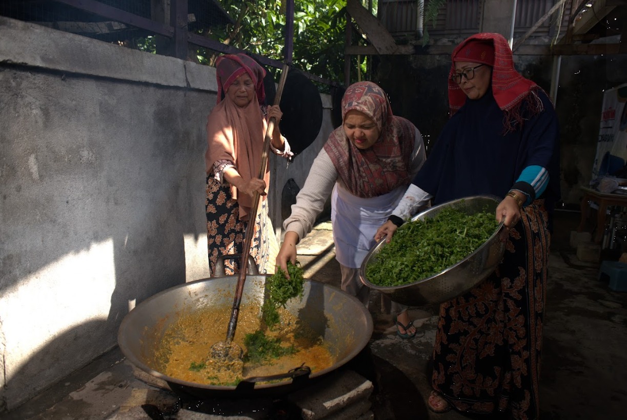 Memasukkan daun paku sebagai bahan utama ke dalam campuran santan, bumbu rendang, dan ikan yang telah diolah menjadi satu. Proses awal dalam pembuatan Rendang Paku. Foto oleh Rekam Indonesia/GNFI