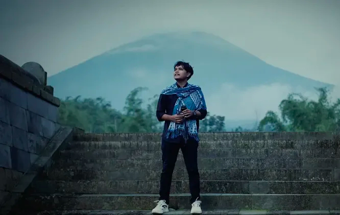 Sofi Ahmad berdiri di tangga batu dengan gunung berkabut di belakang sinar harapan terpancar dari pandangannya.
