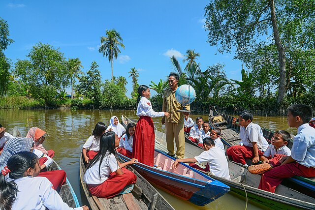 Para siswa di SDN 10 Basirih, Banjarmasin, saat sedang menjalani proses belajar di atas perahu. Pelajaran yang diajarkan oleh guru mereka adalah tentang mengenal dunia (Foto: commons.wikimedia.org/Ryan Dhika Nugraha)