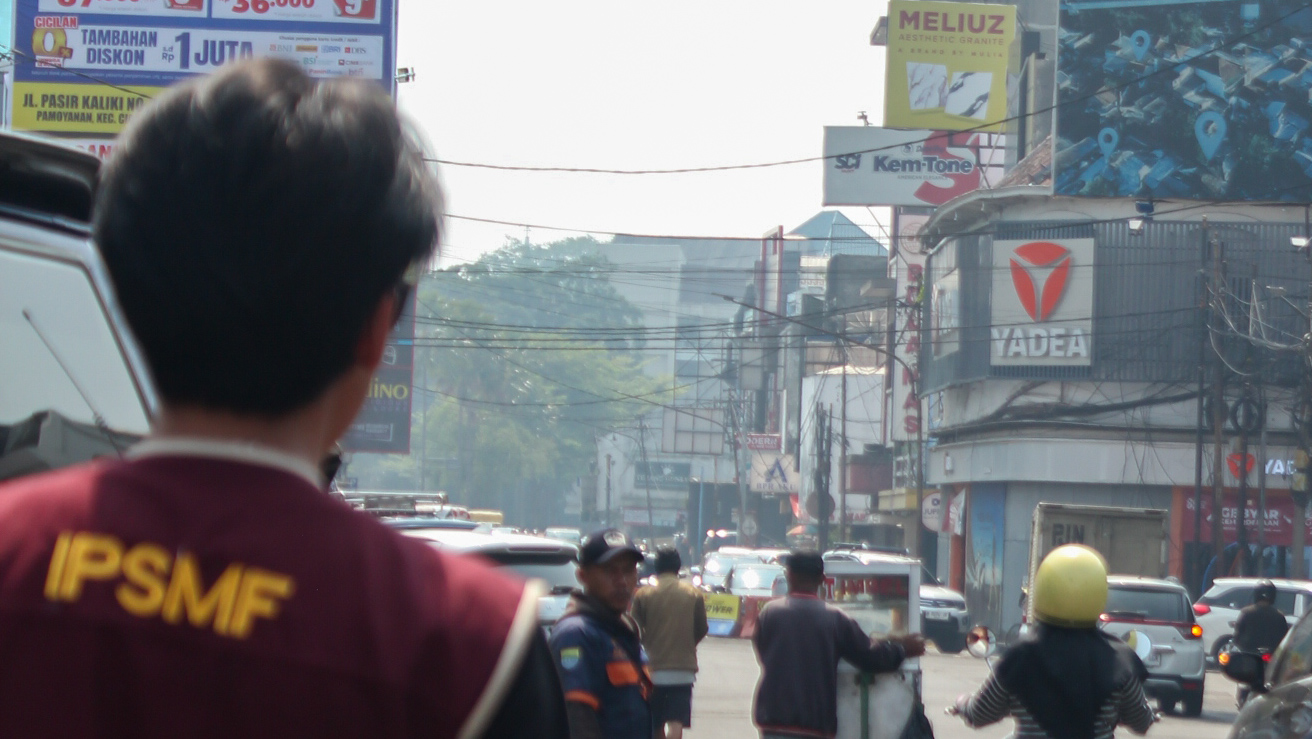 Seorang panitia berbaju rompi IPSMF 2026 tampak belakang sedang memantau suasana jalanan dan lalu lintas pertokoan tua di Route Hunting A Bandung