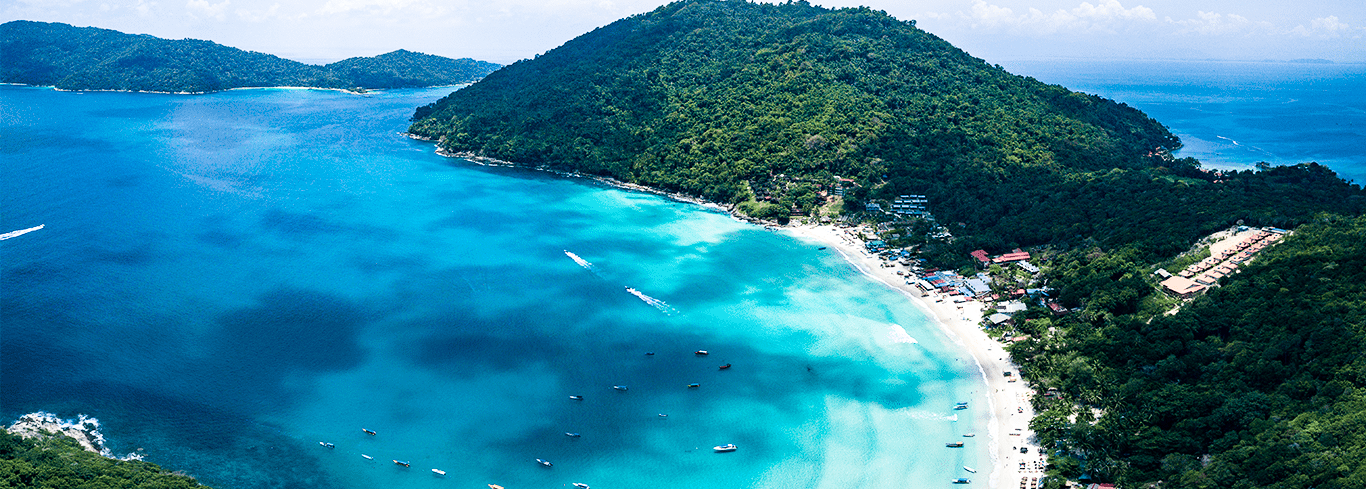 Aerial view of Perhentian Island, Malaysia, showing turquoise waters, boats, and lush green hills.